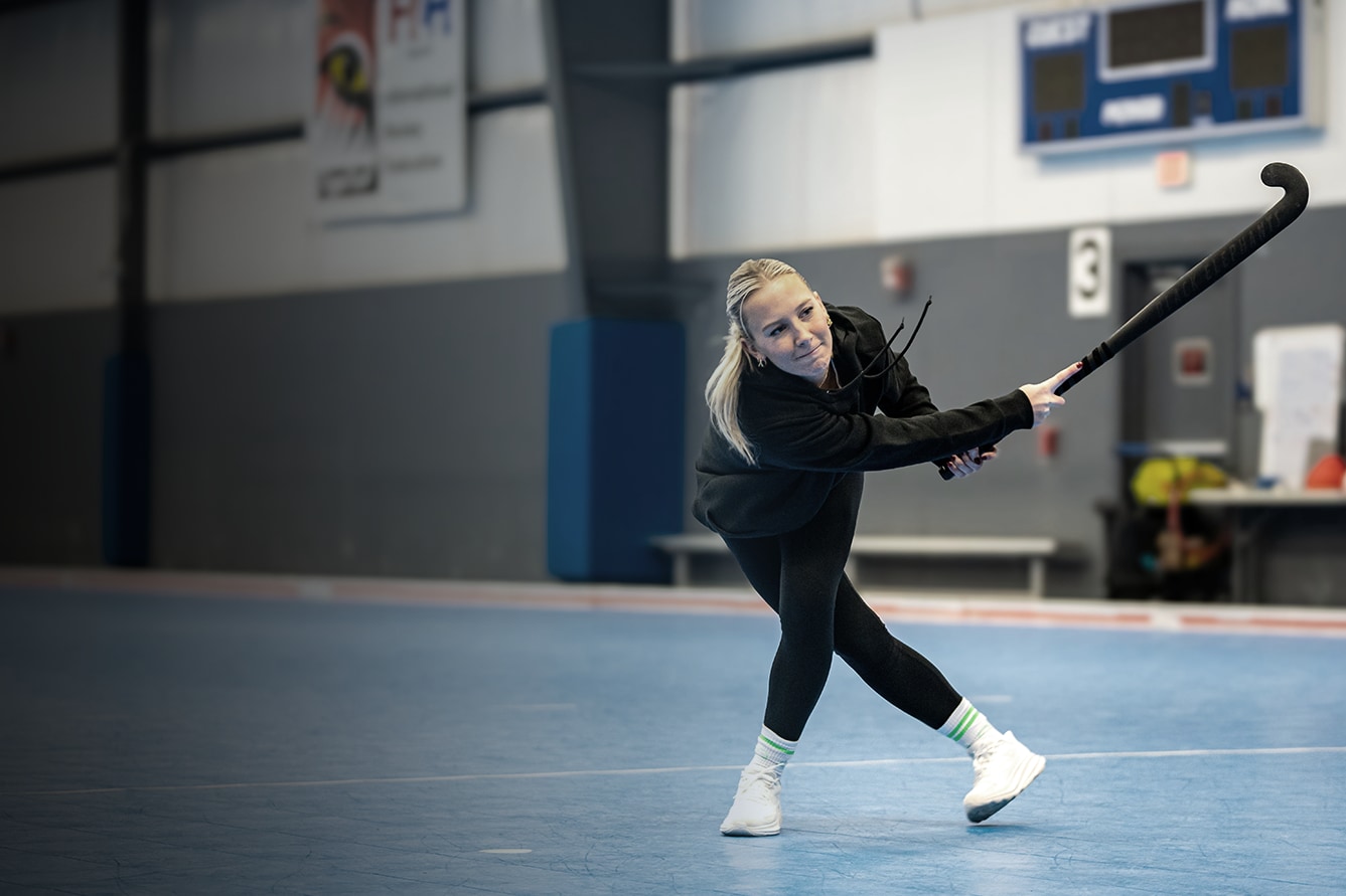 Women play field hockey in an arena